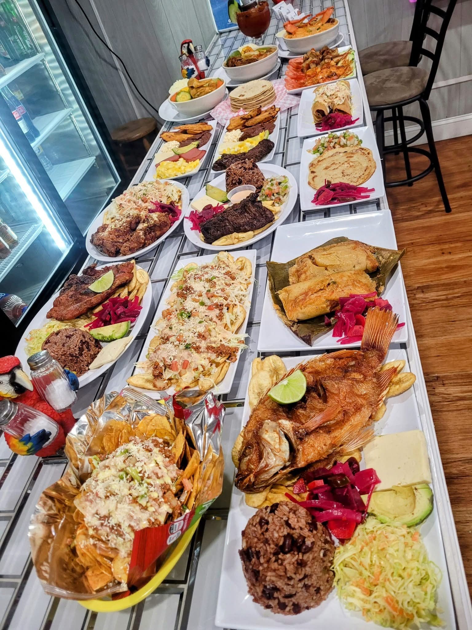 Diverse Latin American dishes including whole fried fish and tamales on a long table.