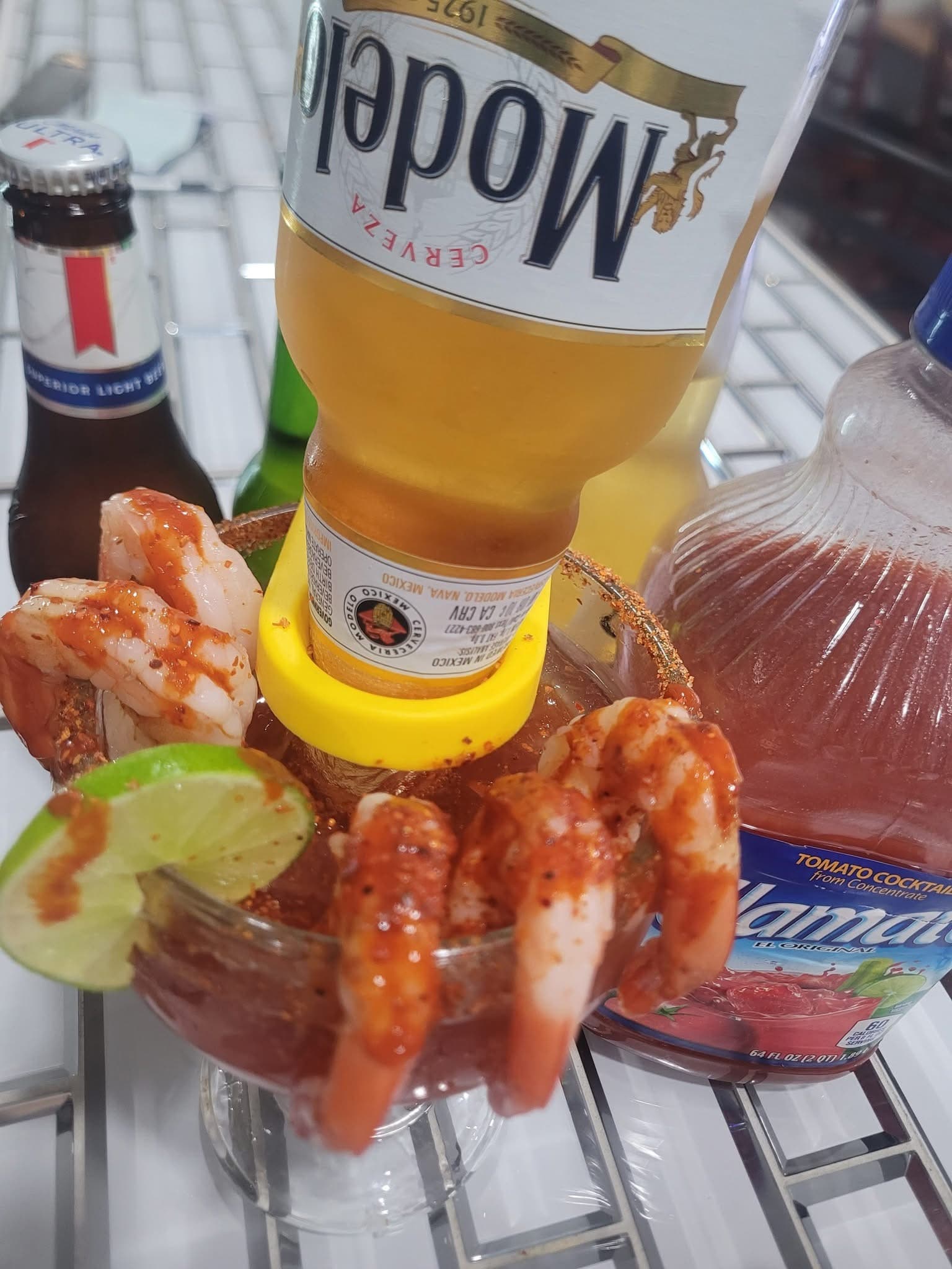 Michelada cocktail garnished with chili-seasoned shrimp, lime, and an inverted Modelo beer bottle.