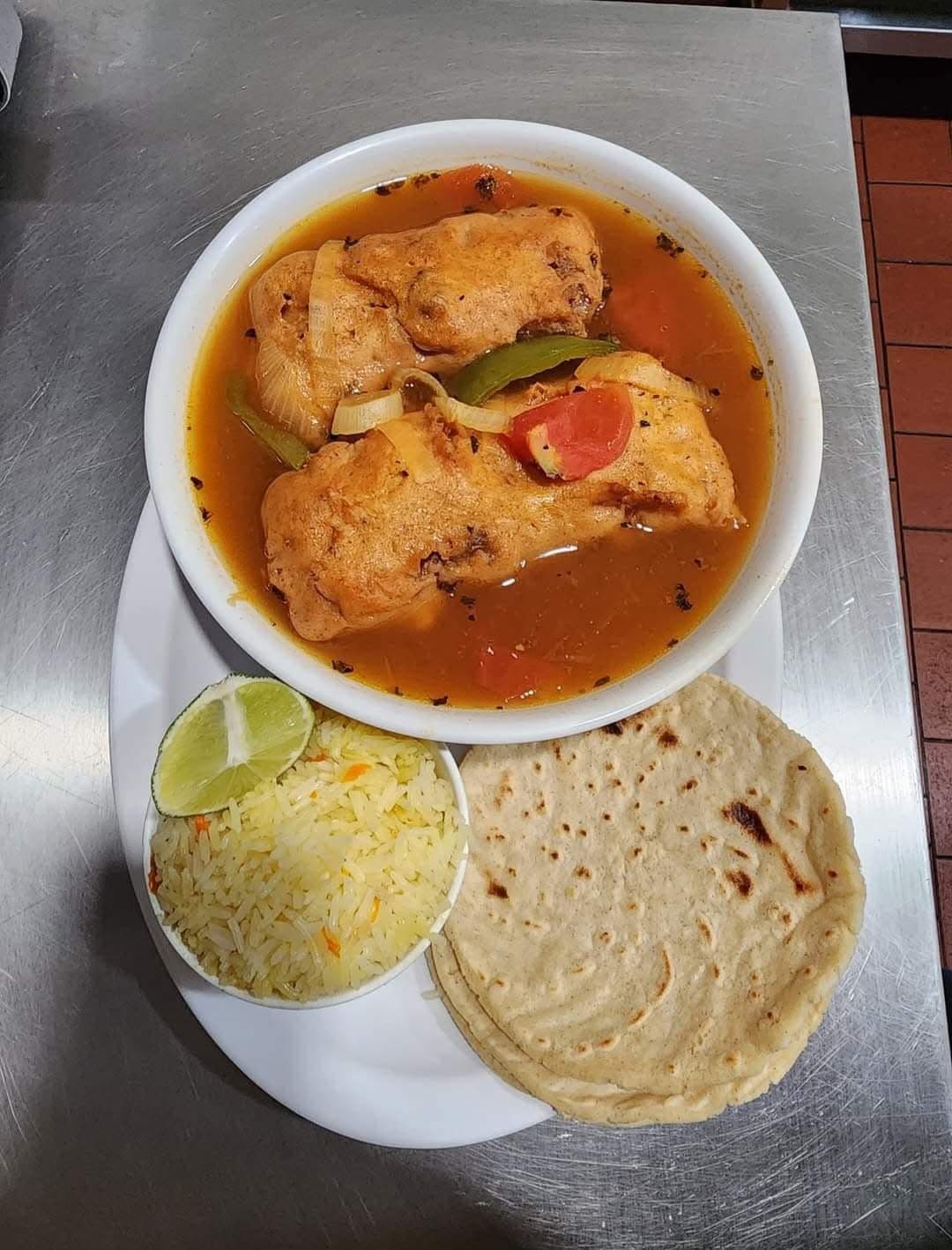 Two stuffed peppers in savory broth served with yellow rice, lime, and handmade corn tortillas.