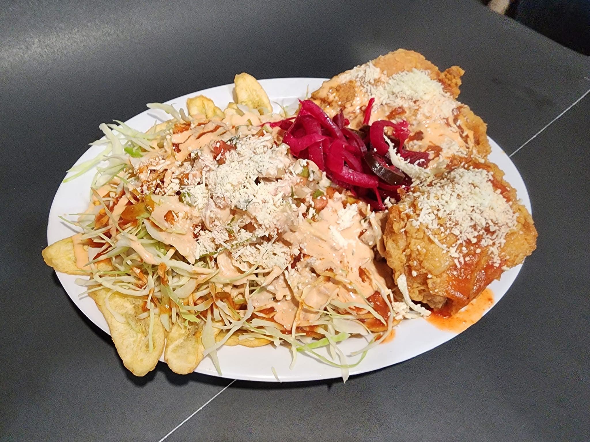 Fried chicken and plantains topped with cabbage, pickled onions, creamy sauce, and crumbled white cheese.