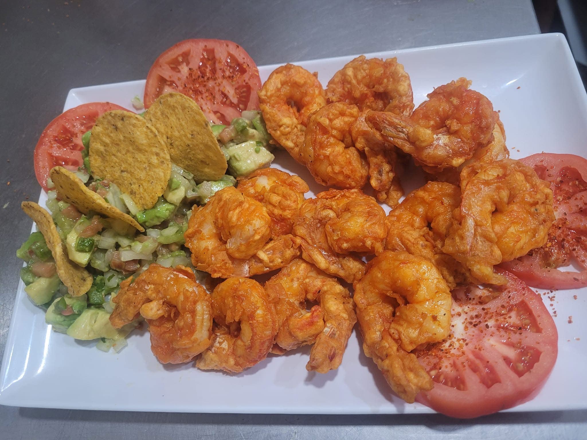 Golden fried shrimp with fresh guacamole, tortilla chips, and seasoned tomato slices on a plate.