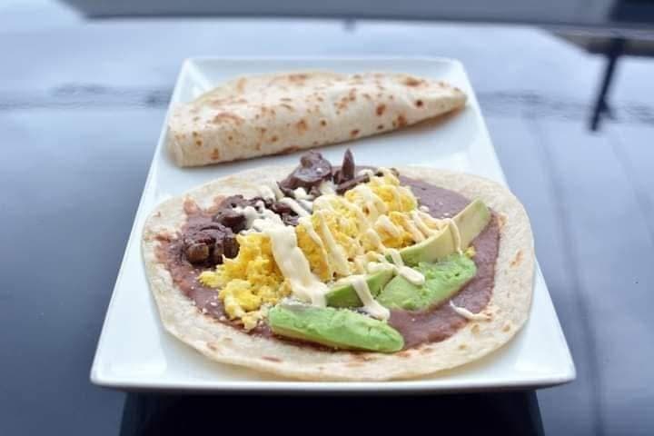 Two flour tortillas on a plate, one topped with eggs, avocado, beans, and crema.
