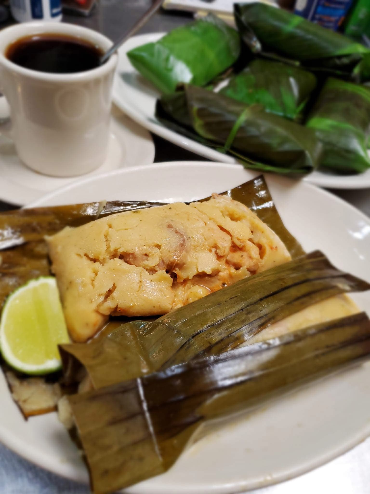 Unwrapped tamale on a banana leaf served with a lime wedge and black coffee.