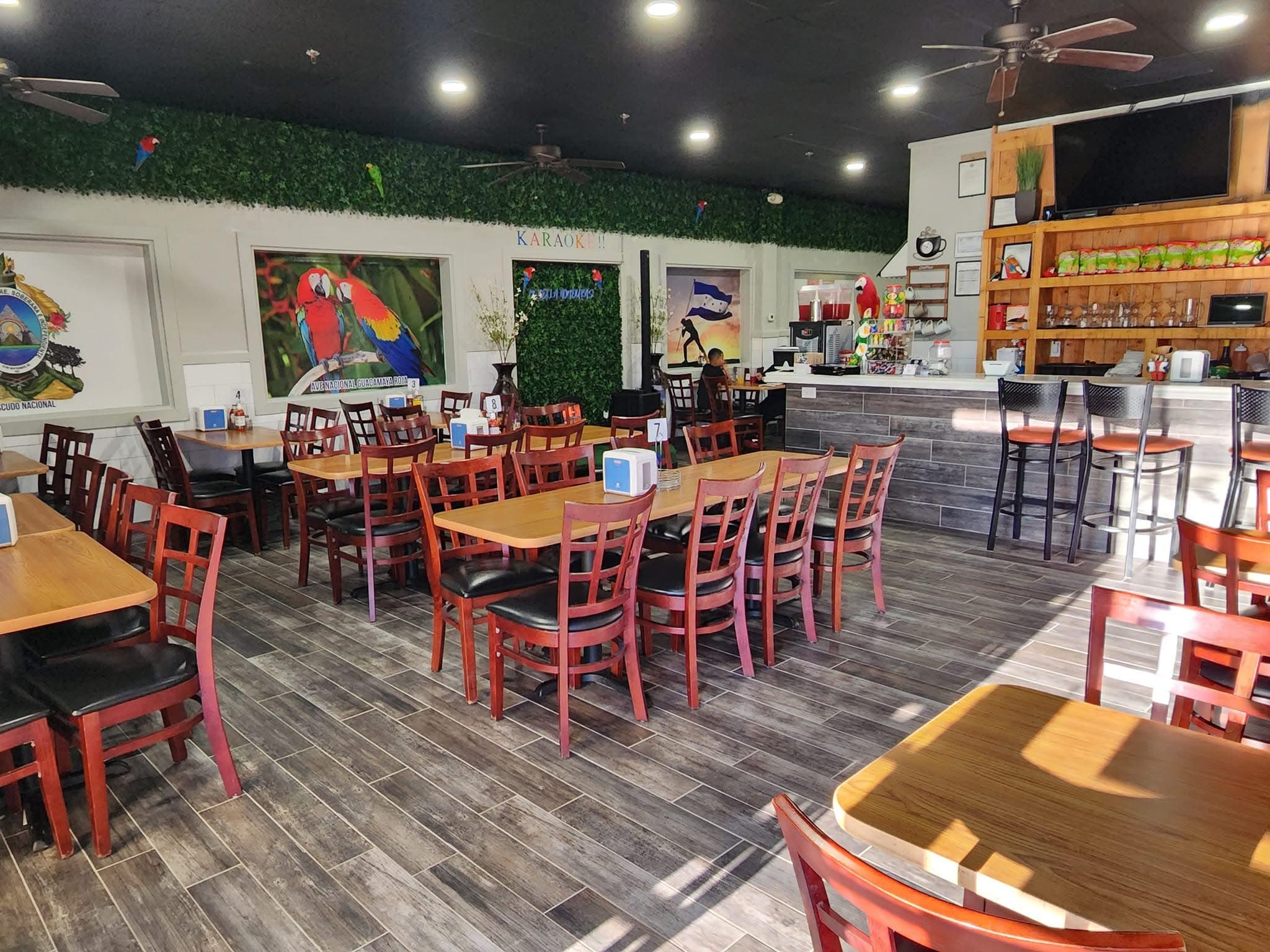 Bright restaurant interior featuring wooden tables, chairs, bar stools, and colorful parrot wall art.