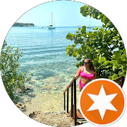 Woman in pink bikini on stairs overlooking clear turquoise water with sailboats in background.